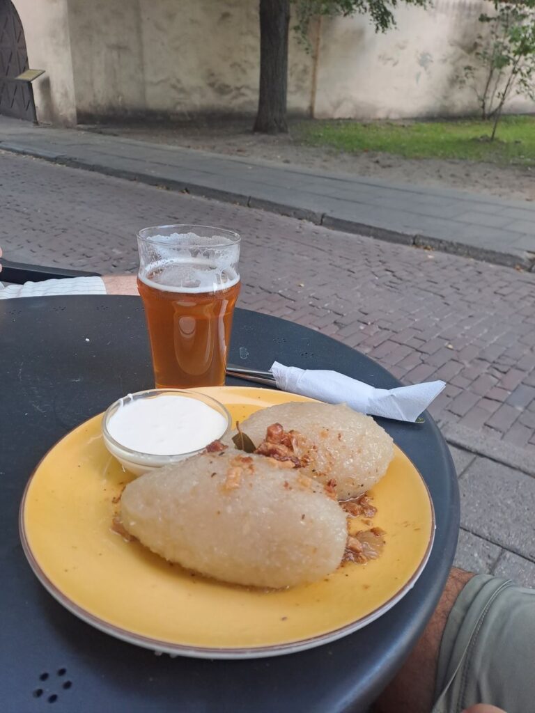 Due cepelinai con spirgučiai e panna acida accanto a una birra, a un tavolino di Vilnius